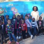 Ms Martha Reads in front of van with children
