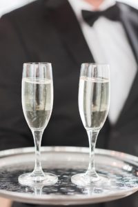 image of a waiter wearing a black tux serving two champagne glasses
